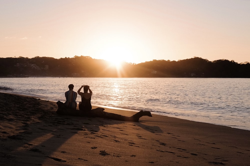 two people sitting on the beach at sunset