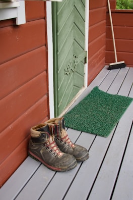 Hiking boots resting on a rustic wooden porch overlooking a forest trail.