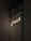 A group of Edison-style light bulbs are illuminated against a dark, textured brick wall. There are leafy plants interwoven with a metal mesh at the top of the image, adding a touch of greenery. The lighting creates a warm, intimate ambiance.