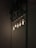 A group of Edison-style light bulbs are illuminated against a dark, textured brick wall. There are leafy plants interwoven with a metal mesh at the top of the image, adding a touch of greenery. The lighting creates a warm, intimate ambiance.