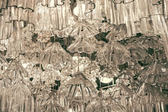 Numerous intricately designed glass light fixtures hanging closely together, creating an ornate and luxurious appearance. The overlapping glass elements form a visually complex pattern with light emanating from within.