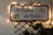 A festive sign with the phrase 'El Taller de Cartas' is adorned with twinkling lights, creating a warm and inviting atmosphere. The sign is mounted on a lattice frame with greenery, and decorated with images of envelopes, suggesting a theme related to letters or correspondence.