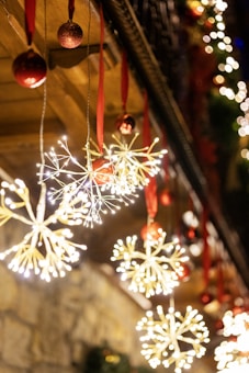 Festive lights in the shape of snowflakes hang from the ceiling, adorned with red ribbons and complemented by red baubles. The warm, glowing lights contrast against the dark background, creating a magical and cozy atmosphere.