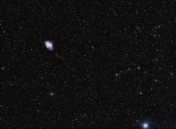 A vast starfield with a distant nebula emitting vibrant purple and blue hues