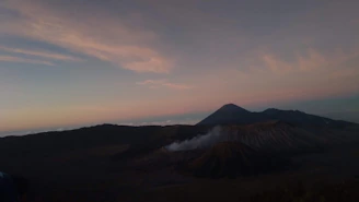 A sprawling Minecraft landscape from the 2b2t server, featuring rugged terrain and player-built structures under a sunset sky.