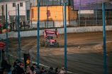 Excited spectators cheering from the stands beside the dirt kart track at 221 Speedway.