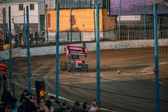 A sprint car roaring around a dirt track under bright stadium lights, kicking up clouds of dust.