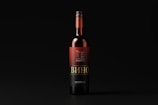 A wine bottle with a black and red label stands upright against a dark background. The label features intricate typography and design elements, with the word 'Вино' prominently displayed.