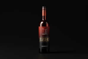 A wine bottle with a black and red label stands upright against a dark background. The label features intricate typography and design elements, with the word 'Вино' prominently displayed.
