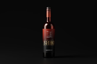 A wine bottle with a black and red label stands upright against a dark background. The label features intricate typography and design elements, with the word 'Вино' prominently displayed.