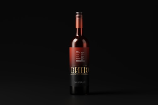 A wine bottle with a black and red label stands upright against a dark background. The label features intricate typography and design elements, with the word 'Вино' prominently displayed.