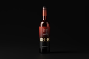 A wine bottle with a black and red label stands upright against a dark background. The label features intricate typography and design elements, with the word 'Вино' prominently displayed.
