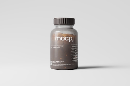 A transparent brown plastic pill bottle with a dark cap is placed against a light gray background. The label on the bottle reads 'mocp' and includes additional text and a website link at the bottom. The bottle's contents appear to be small brown pills.