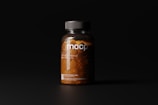 A dark-toned image showcasing a clear plastic bottle filled with orange pills under soft lighting. The bottle has a black cap and features minimalist labeling with the letters 'mocp' prominently displayed.