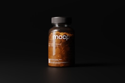 A dark-toned image showcasing a clear plastic bottle filled with orange pills under soft lighting. The bottle has a black cap and features minimalist labeling with the letters 'mocp' prominently displayed.