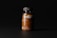 A dark-toned image showcasing a clear plastic bottle filled with orange pills under soft lighting. The bottle has a black cap and features minimalist labeling with the letters 'mocp' prominently displayed.