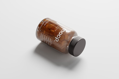 A transparent bottle lies on its side on a plain white surface. The bottle contains several round, orange tablets and has a dark-colored cap. The label on the bottle displays the word 'nocop' and some small text.