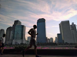 An action shot of someone jogging in customized shorts and a bright t-shirt, with a blurred cityscape behind.