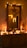 A warmly lit room featuring a decorated mirror with string lights and a star ornament. The wooden dresser below is adorned with festive decorations, including small candles, a miniature Christmas tree, and decorative figurines. The ambient glow creates a cozy and inviting atmosphere.