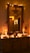 A warmly lit room featuring a decorated mirror with string lights and a star ornament. The wooden dresser below is adorned with festive decorations, including small candles, a miniature Christmas tree, and decorative figurines. The ambient glow creates a cozy and inviting atmosphere.