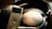 A pair of black Sony headphones is resting next to a silver iPod. The headphones have a cushioned headband and large ear cups, with the Sony logo prominently displayed. The iPod has a screen displaying music with a circular control pad below it.