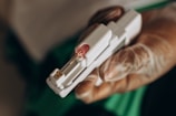 A hand wearing a latex glove is holding a medical device with a small needle and a pink-colored cap.