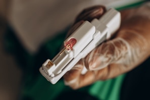 A hand wearing a latex glove is holding a medical device with a small needle and a pink-colored cap.