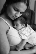 A serene scene of a woman gently cradling a newborn baby against her chest. The baby is peacefully asleep, close to the mother's heart, creating an intimate and tender moment. The black-and-white tones add a timeless and classic feel to the image.