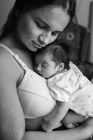 A serene scene of a woman gently cradling a newborn baby against her chest. The baby is peacefully asleep, close to the mother's heart, creating an intimate and tender moment. The black-and-white tones add a timeless and classic feel to the image.