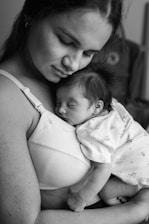 A serene scene of a woman gently cradling a newborn baby against her chest. The baby is peacefully asleep, close to the mother's heart, creating an intimate and tender moment. The black-and-white tones add a timeless and classic feel to the image.