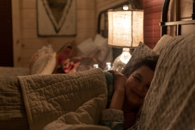 Woman relaxing in bed under a heated plaid, blue glacier light subtly glowing, creating a cozy atmosphere.