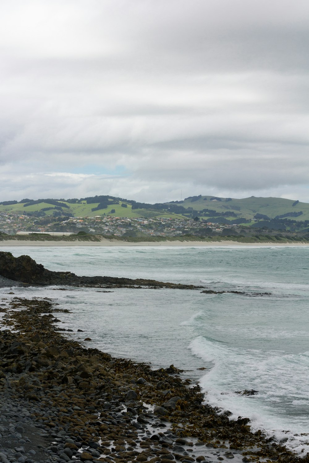 a rocky beach with a body of water and hills in the background