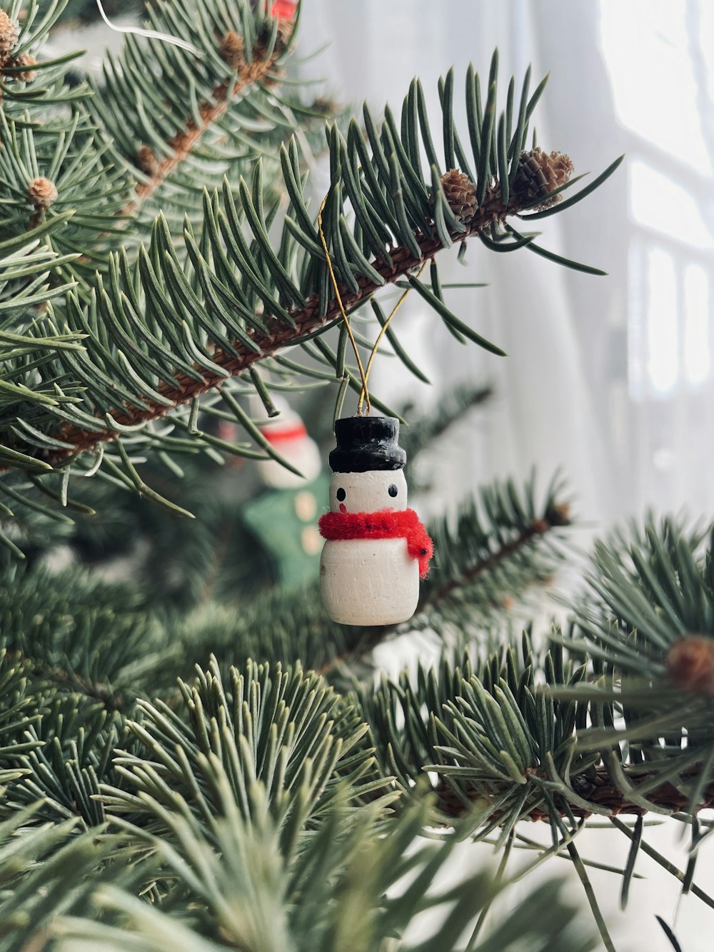 a snowman ornament hanging from a pine tree
