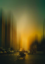 A focused delivery motorcyclist riding through city streets during sunset.