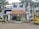 The image depicts the main entrance of a medical college and hospital, which has the name 'Tagore Medical College & Hospital' prominently displayed above the doorway. The building is a white multi-story structure with a clean, organized appearance, flanked by some trees and greenery. A yellow college bus with the name 'Tagore College Bus' is parked on the right side. A few potted plants and decorative pillars are present around the entrance.