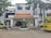 The image depicts the main entrance of a medical college and hospital, which has the name 'Tagore Medical College & Hospital' prominently displayed above the doorway. The building is a white multi-story structure with a clean, organized appearance, flanked by some trees and greenery. A yellow college bus with the name 'Tagore College Bus' is parked on the right side. A few potted plants and decorative pillars are present around the entrance.
