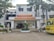 The image depicts the main entrance of a medical college and hospital, which has the name 'Tagore Medical College & Hospital' prominently displayed above the doorway. The building is a white multi-story structure with a clean, organized appearance, flanked by some trees and greenery. A yellow college bus with the name 'Tagore College Bus' is parked on the right side. A few potted plants and decorative pillars are present around the entrance.