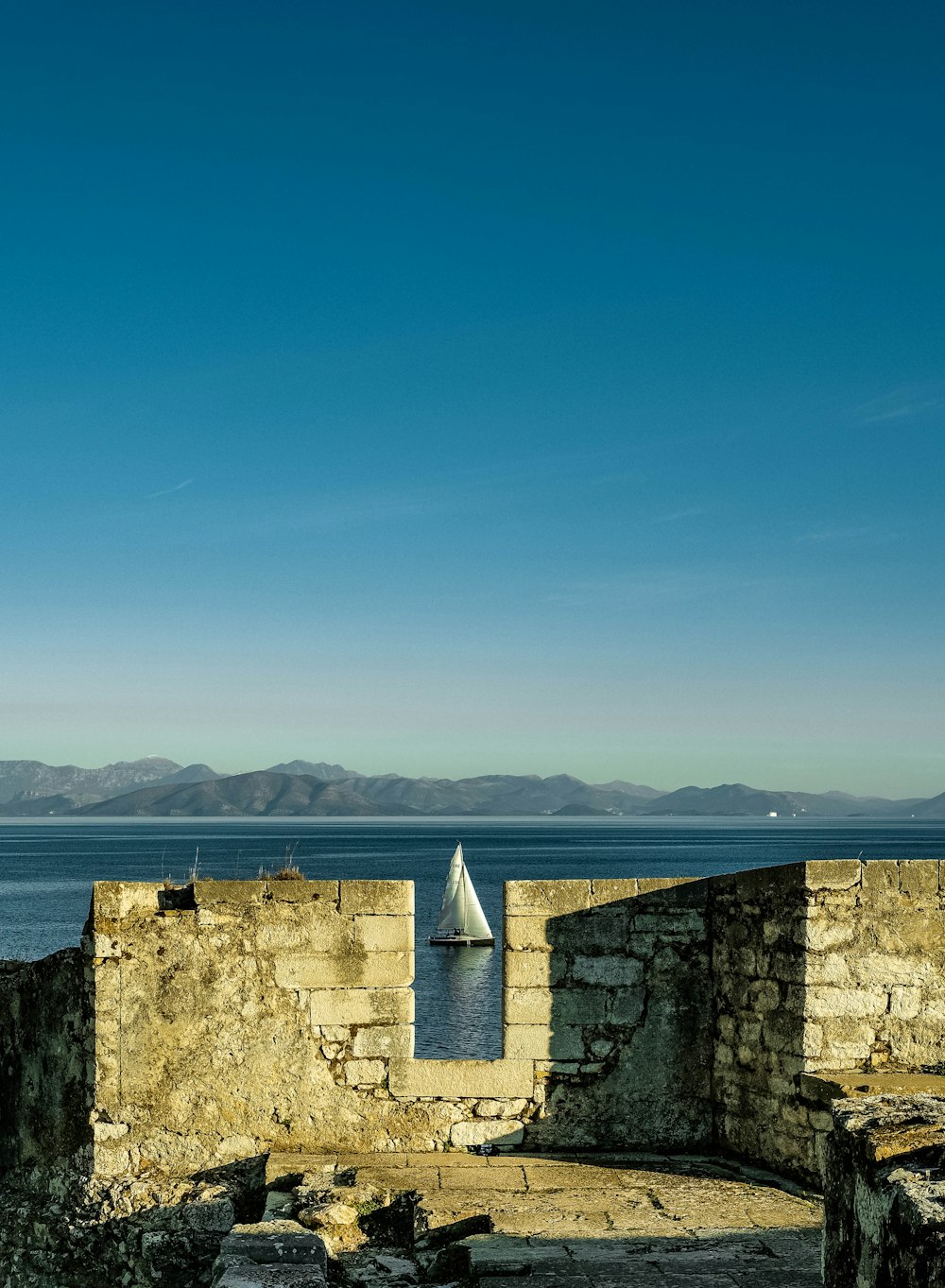 a sailboat floating in the water near a stone wall