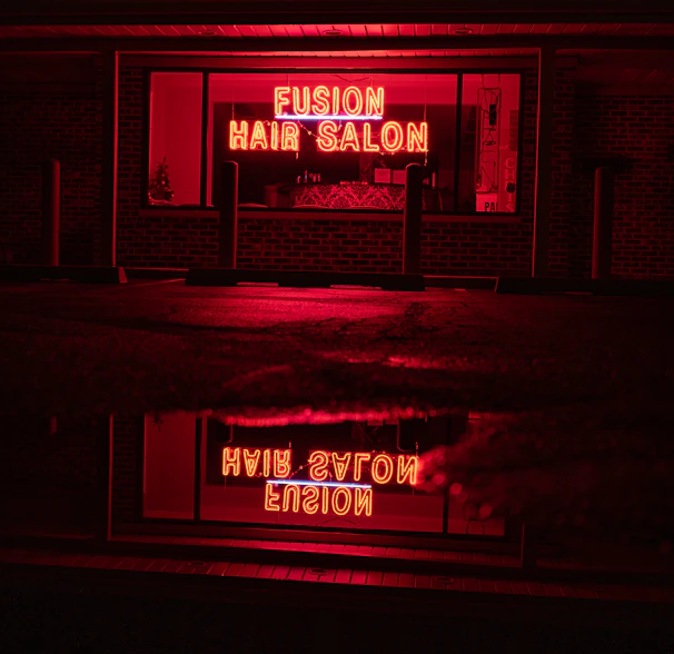 A beauty salon storefront illuminated by a bold burnt-orange neon sign at night