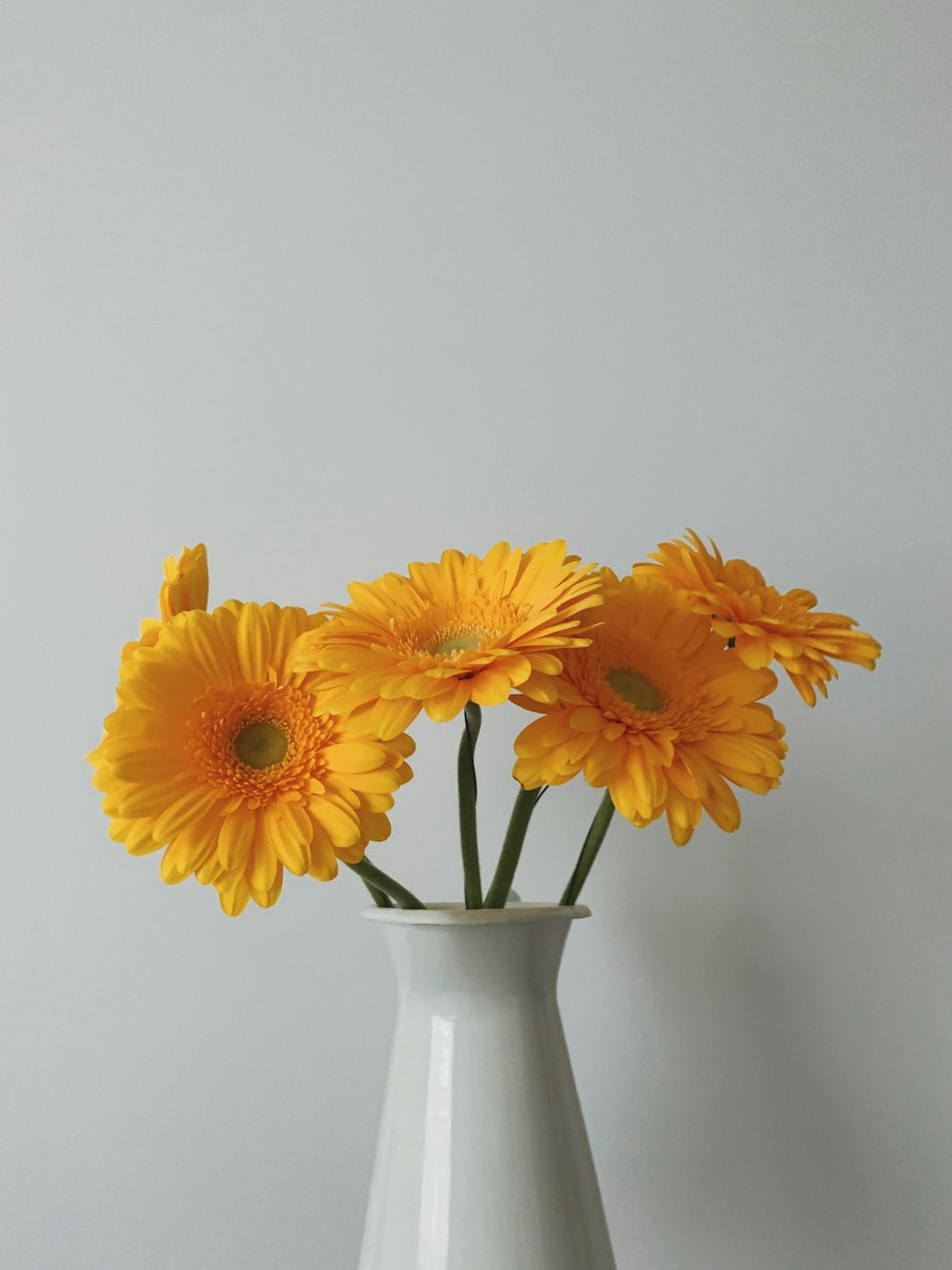 a white vase filled with yellow flowers on top of a table