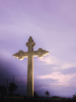 A peaceful countryside cross standing tall against a vibrant sky at dusk.