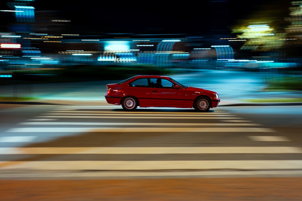 a red car driving down a street at night