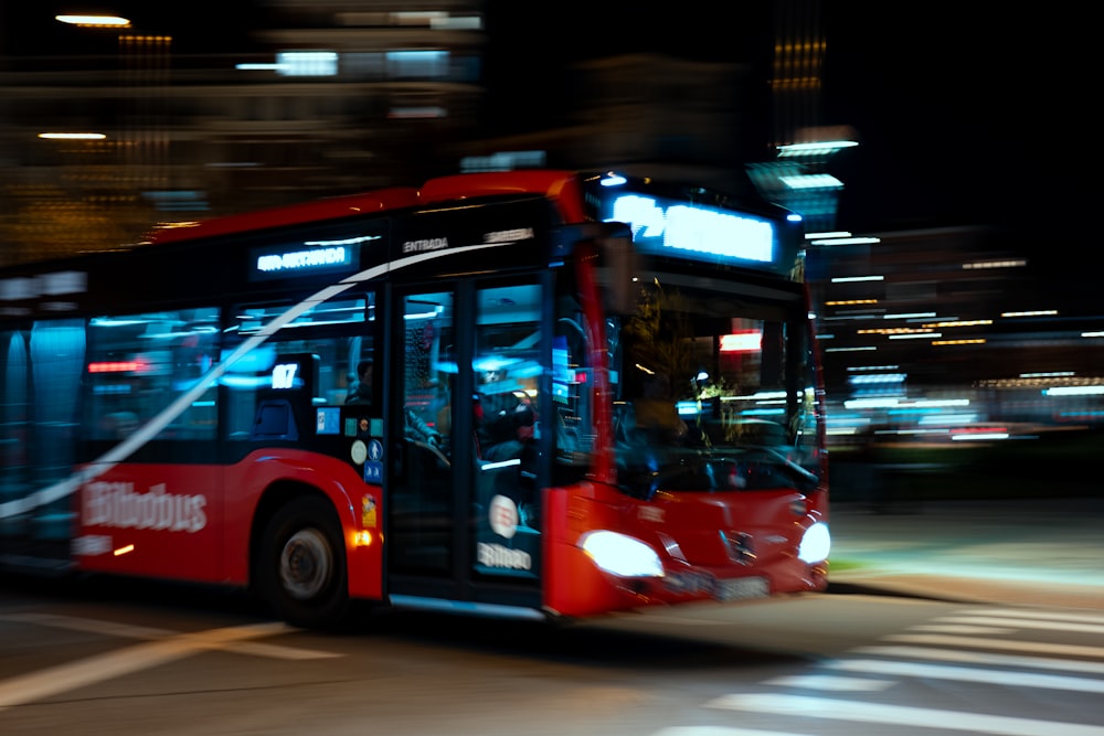 a red bus driving down a street at night