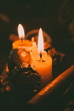 Two lit candles with warm yellow flames stand amidst decorative pine cones and cinnamon sticks, creating an intimate and cozy ambiance.