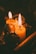 Two lit candles with warm yellow flames stand amidst decorative pine cones and cinnamon sticks, creating an intimate and cozy ambiance.