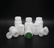 A group of white plastic bottles with various shapes and sizes are arranged on a dark background. Some bottles have screw caps, while others have flip-top lids. The center bottle features a green cap, standing out among the predominantly white lids.