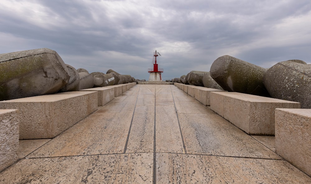 a walkway with large rocks and a lighthouse in the distance