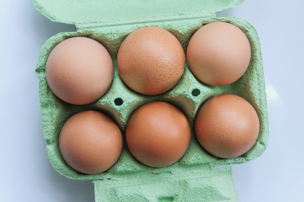 six eggs in a carton on a white surface