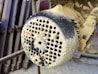 A close-up view of a heavily dust-covered industrial machine part with perforations. The surface appears coarse and textured, with layers of fine dust or sawdust accumulated.