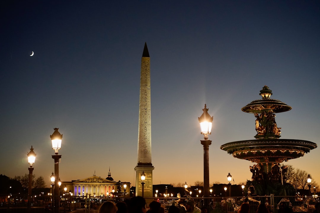a group of people standing around a fountain at night, PLACE DE LA CONCORDE / PARIS / FRANCE